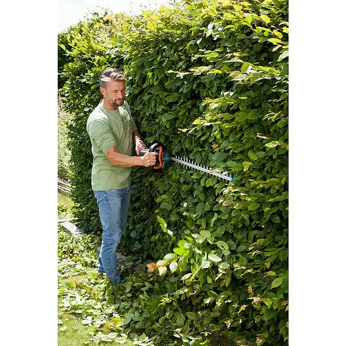 Gardena PowerCut Elektro-Heckenschere 700/65 - 700 W, Schnittlänge: 65 cm - Ein Mann schneidet eine Hecke mit einer Gardena Heckenschere, um seinen Garten in Ordnung zu halten. Das Gerät ist leicht und benutzerfreundlich.
