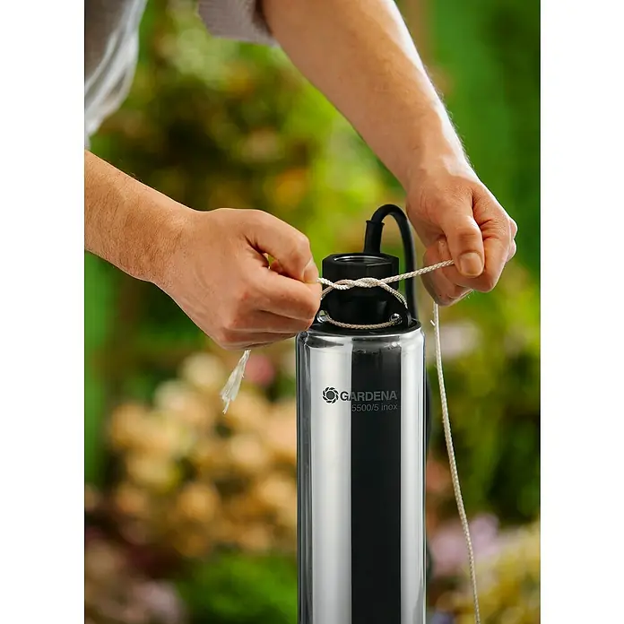 Gardena Tiefbrunnenpumpe 5500/5 Inox - 850 W, 5.500 l/h, Edelstahl - Nahaufnahme einer Person, die ein Seil an einer GARDENA 5500/5 inox Gartenpumpe befestigt.