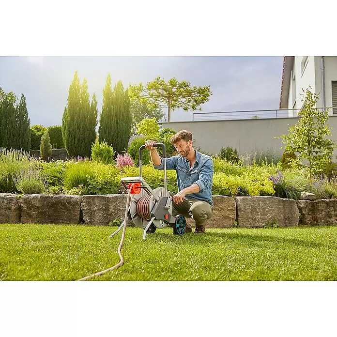 Gardena Schlauchwagen-Set CleverRoll M - Kunststoff/Metall, Schlauchlänge: 25 m - Mann im Garten bedient einen grau-orangen Schlauchwagen mit rotem Schlauch.