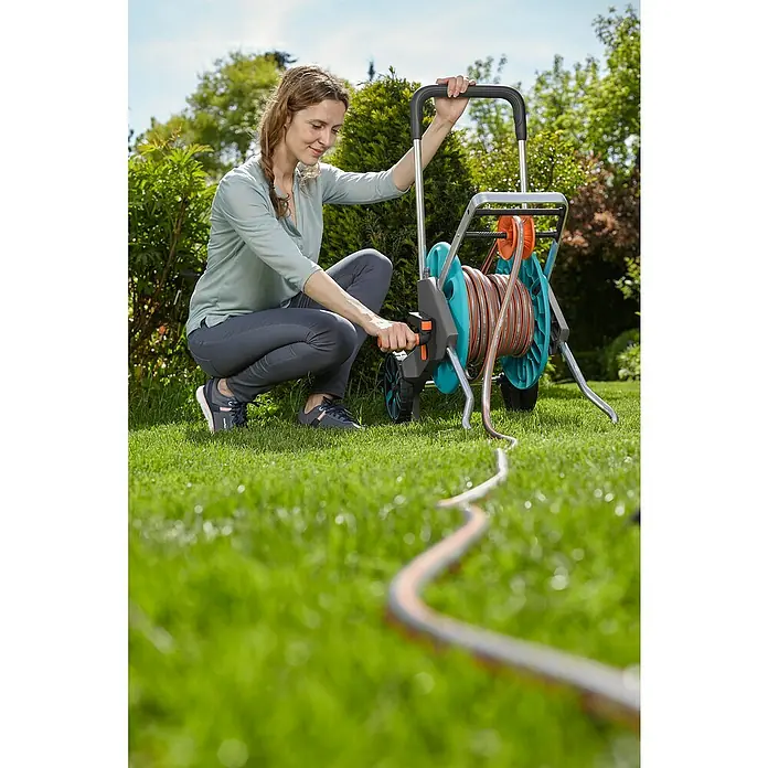 Gardena Schlauchwagen-Set CleverRoll M Easy Set - Kunststoff/Metall, Schlauchlänge: 20 m - Frau benutzt eine Gardena Schlauchtrommel mit Schlauch auf einer grünen Wiese, um ihren Garten zu bewässern.