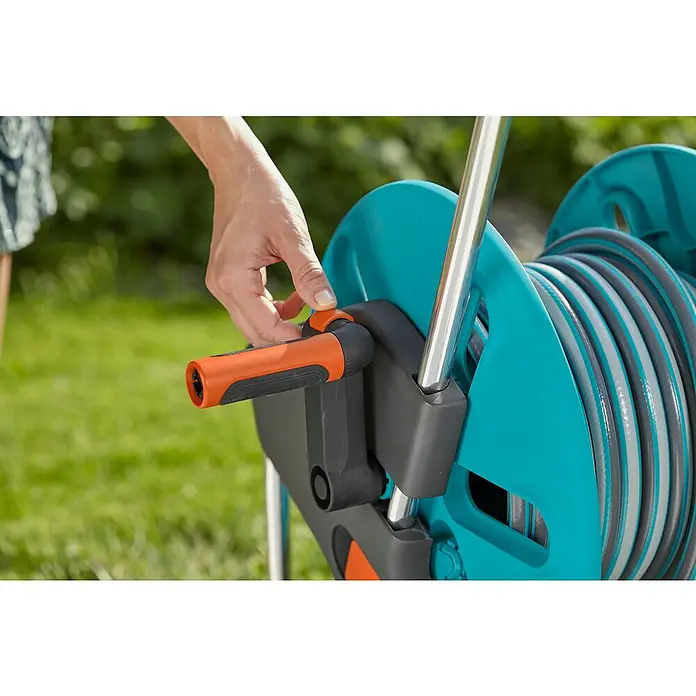 Gardena Schlauchwagen CleverRoll M - Kunststoff/Metall, Schlauchkapazität: 60 m, 13 mm (½″) - Eine Person bedient eine AquaRoll Gartenschlauchhaspel mit einer Handkurbel, um den Schlauch aufzurollen.