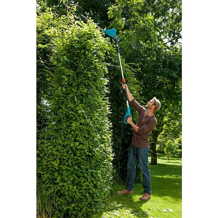 Gardena Teleskop-Heckenschere THS 500/48 - 500 W, Schwertlänge: 48 cm - Mann schneidet mit einer Gardena Akku-Teleskop-Heckenschere eine hohe Hecke im Garten. Das Gerät ermöglicht bequemes Arbeiten in der Höhe.
