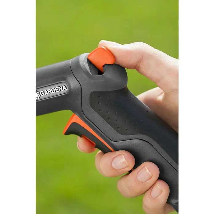 Gardena Premium Brause - 2 -tlg., Kunststoff - Nahaufnahme einer Hand, die einen Gardena-Gartenschlauch mit orangefarbenem Auslöser bedient, vor grünem Hintergrund.