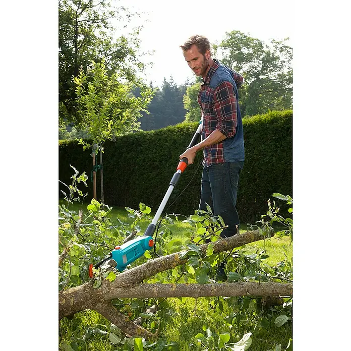 Gardena Elektro-Hochentaster TCS 720/20 - Teleskopstiel - Ein Mann benutzt eine Gardena Akku-Astsäge, um Äste im Garten zu schneiden. Sie ist hellblau mit orangen Akzenten und einem Teleskopstiel.