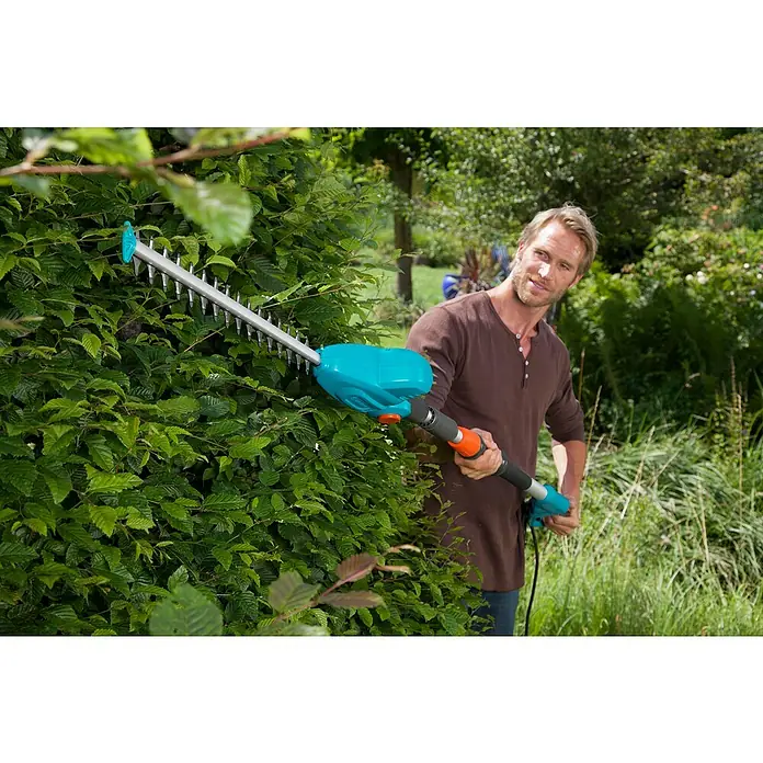 Gardena Teleskop-Heckenschere THS 500/48 - 500 W, Schwertlänge: 48 cm - Mann schneidet mit einer Gardena-Akku-Teleskop-Heckenschere eine Hecke im Garten. Das Gerät ist türkis und grau.