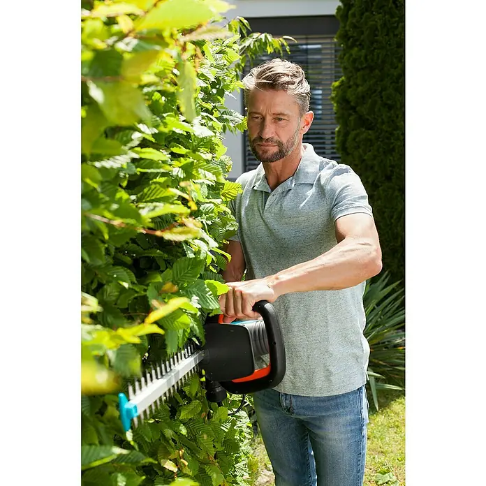 Gardena ComfortCut Elektro-Heckenschere 600/55 - 600 W, Schnittlänge: 55 cm - Mann schneidet Hecke mit Gardena Heckenschere. Die Heckenschere ist schwarz und orange und hat ein blaues Ende.
