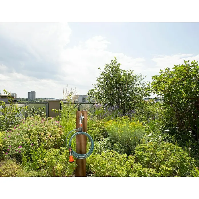 Gardena City Gardening Spiralschlauch - Länge: 7,5 m - Außenaufnahme einer Gardena Gartenschlauchbox an einem Holzpfosten inmitten üppiger Vegetation, ideal zur Gartenbewässerung.