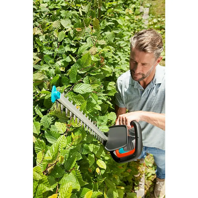 Gardena ComfortCut Elektro-Heckenschere 600/55 - 600 W, Schnittlänge: 55 cm - Ein Mann benutzt eine Gardena Heckenschere, um eine grüne Hecke zu trimmen, wobei die Klingen und der Griff der Schere im Fokus stehen.