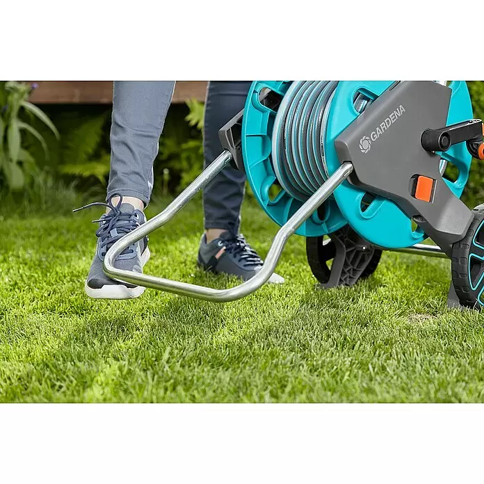 Gardena Schlauchwagen CleverRoll M - Kunststoff/Metall, Schlauchkapazität: 60 m, 13 mm (½″) - Gardena Schlauchwagen mit Schlauch, türkis und grau, im Freien von einer Person bedient.