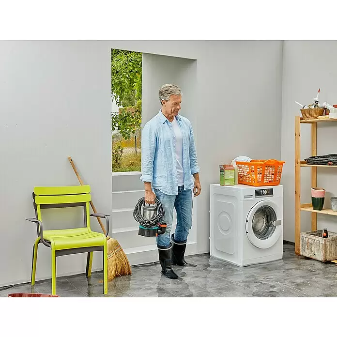 Gardena Klarwasser-Tauchpumpe 11000 Aquasensor - 450 W, Max. Fördermenge: 11.000 l/h - Ein Mann in Stiefeln hält eine Gardena Wasserpumpe in einem überfluteten Raum, bereit zum Wasserabpumpen.