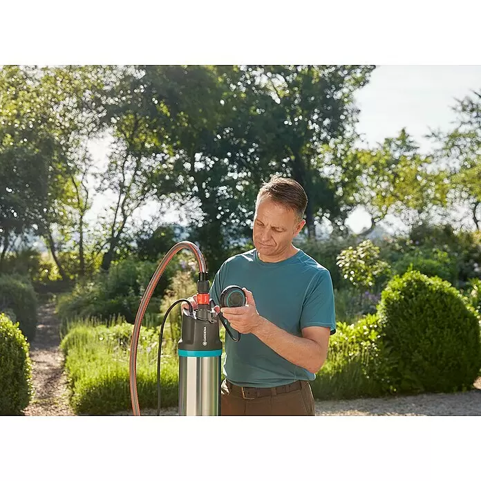 Gardena Drucktauchpumpe 5900/4 Inox - 900 W, Max. Fördermenge: 5.900 l/h - Mann hält schwarz/blaue Gardena Pumpen-Steuereinheit, verbunden mit silberner Tauchpumpe im Garten.