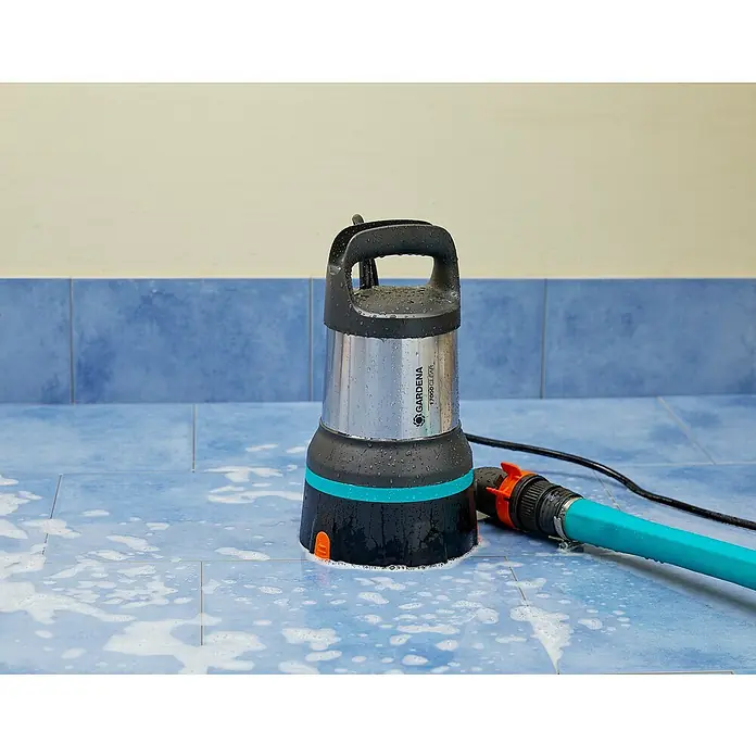 Gardena Bomba de achique sumergible para agua limpia 17000 Aquasensor - 750 W, Capacidad de bombeo máx.: 17.000 l/h - Una bomba de agua sucia Gardena con una manguera azul se encuentra sobre una superficie alicatada y está cubierta de gotas de agua.