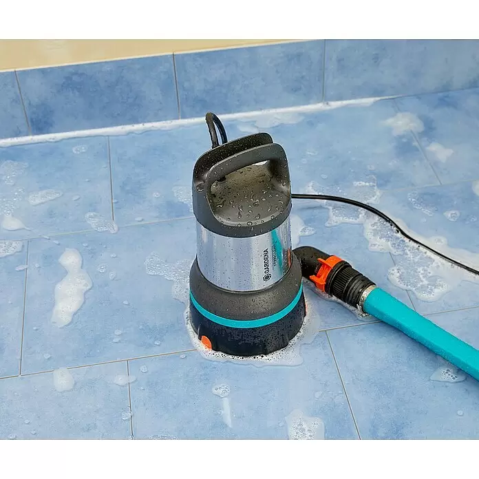 Gardena Bomba de achique sumergible para agua limpia 17000 Aquasensor - 750 W, Capacidad de bombeo máx.: 17.000 l/h - Una bomba sumergible Gardena húmeda (plateada, negra, turquesa) con una manguera azul en suelo de baldosas azules, con agua jabonosa.