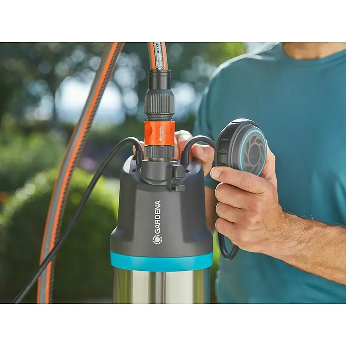 Gardena Drucktauchpumpe 5900/4 Inox - 900 W, Max. Fördermenge: 5.900 l/h - Eine Gardena-Tauchdruckpumpe wird von einer Person bedient. Das Gerät ist grau, blau und silberfarben.