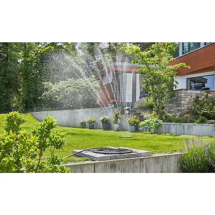 Gardena Tauchpumpe 5900/4 INOX Automatic - 900 W, Max. Fördermenge: 5.900 l/h - Ein Rasensprenger bewässert einen grünen Garten mit Blumen und einem modernen Haus im Hintergrund. Der Fokus liegt auf dem Bewässerungssystem.