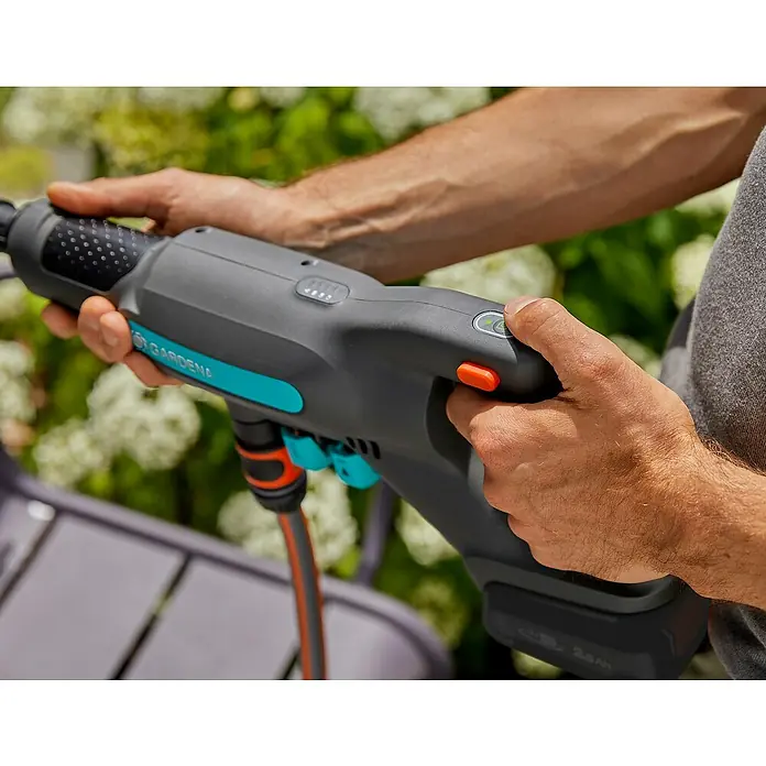 Gardena Power for All 18V Akku-Druckreiniger AquaClean 24/18V SE - 18 V, 1 Akku, 2,5 Ah - Die Gardena Akku-Spritzpistole wird von einer Person gehalten und bedient, vor blühenden Büschen.