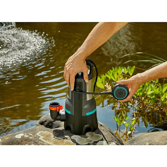 Gardena Schmutzwasserpumpe 25000 - 1.100 W, Max. Fördermenge: 25.000 l/h, Eintauchtiefe: 7 m - Eine Gardena Schmutzwasserpumpe wird an einem Teich platziert, um unerwünschtes Wasser abzupumpen. Praktisches Gerät für den Garteneinsatz.