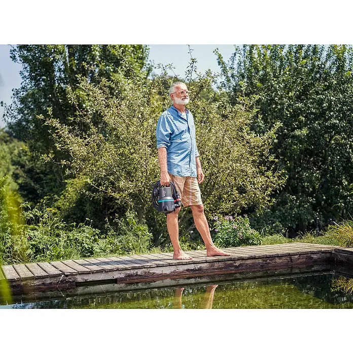 Gardena Schmutzwasserpumpe 9000 - 300 W, Max. Fördermenge: 9.000 l/h, Eintauchtiefe: 7 m - Der Mann steht am Teich und hält eine GARDENA Schmutzwasser-Tauchpumpe 7000/D. Diese Pumpe eignet sich ideal zum Abpumpen von Schmutzwasser.