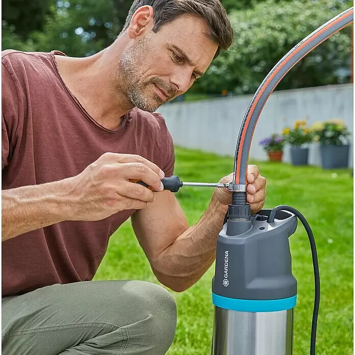 Gardena Tauchpumpe 5900/4 INOX Automatic - 900 W, Max. Fördermenge: 5.900 l/h - Mann schließt einen grau-orangen Schlauch mit einem Schraubenzieher an eine Gardena Pumpe an.