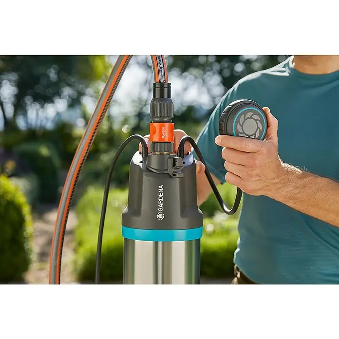 Gardena Bomba sumergible de presión 5900/4 Inox - Capacidad de bombeo máx.: 5.900 l/h, Altura de transporte máx.: 35 m - Primer plano de una bomba de jardín Gardena con conexión de manguera, ideal para riego o drenaje. El hombre sujeta el interruptor de flotador.