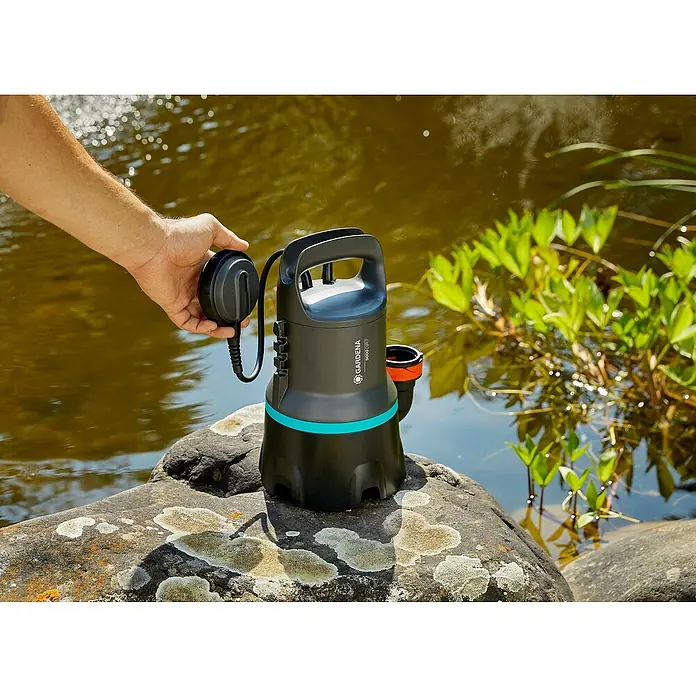 Gardena Schmutzwasserpumpe 9000 - 300 W, Max. Fördermenge: 9.000 l/h, Eintauchtiefe: 7 m - Gardena 9000 Dirt-Schmutzwasserpumpe in Aktion, stehend auf einem Stein neben einem Teich, mit einem Arm, der den Schwimmer hält.