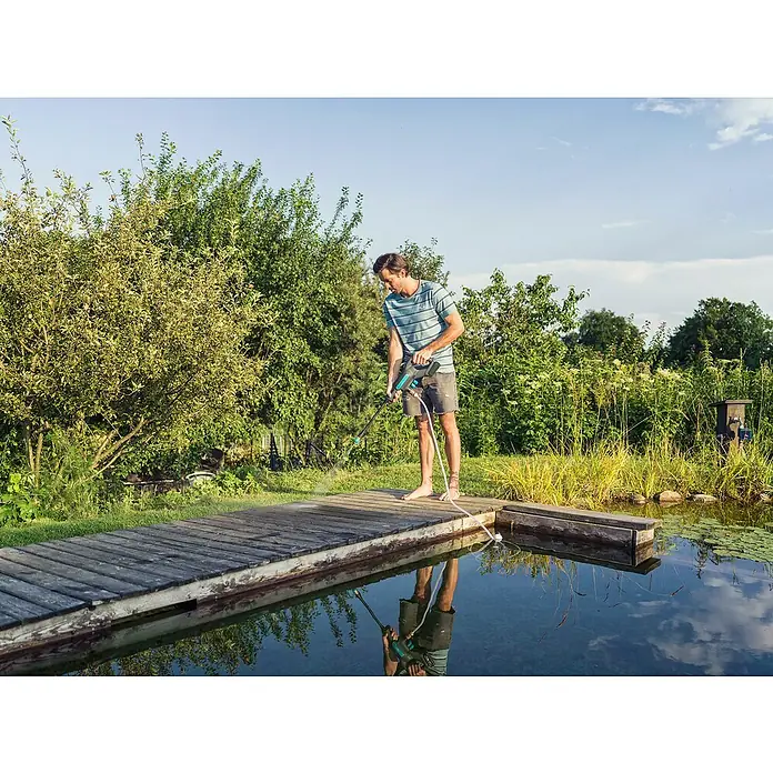 Gardena Power for All 18V Akku-Druckreiniger AquaClean 24/18V SE - 18 V, 1 Akku, 2,5 Ah - Ein Mann reinigt eine Holzterrasse mit einem Gardena Akku-Hochdruckreiniger, der das Wasser aus einem Teich bezieht.