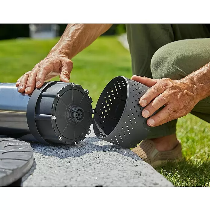 Gardena Tauchpumpe 5900/4 INOX Automatic - 900 W, Max. Fördermenge: 5.900 l/h - Hände montieren eine silberne zylindrische Pumpe mit einem dunkelgrauen perforierten Filterkorb und einem Sternantrieb.