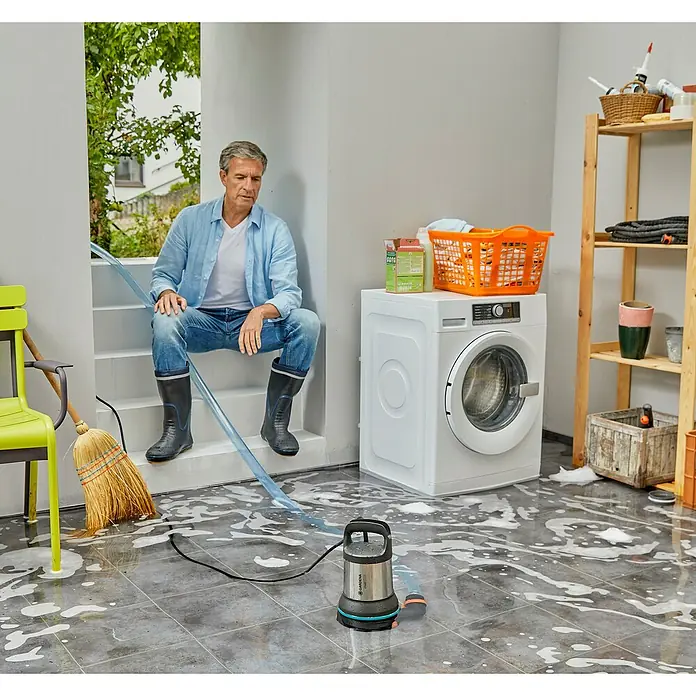 Gardena Klarwasser-Tauchpumpe 17000 Aquasensor - 750 W, Max. Fördermenge: 17.000 l/h - Mann sitzt auf Treppe in überflutetem Raum. Gardena Schmutzwasser-Tauchpumpe fördert Wasser ab, daneben ein Wischmopp und eine Waschmaschine.