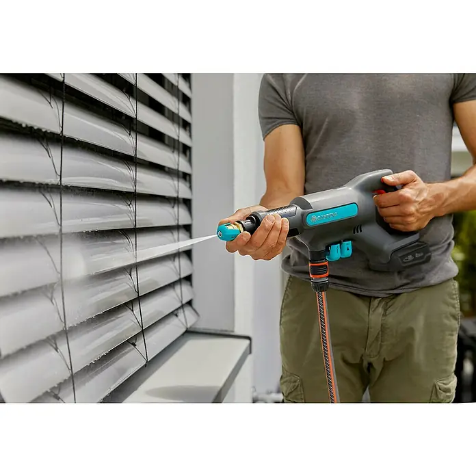 Gardena Power for All 18V Akku-Druckreiniger AquaClean 24/18V PR - 18 V, 1 Akku, 2,5 Ah - Ein Mann reinigt Jalousien mit einem Gardena Akku-Hochdruckreiniger. Das Gerät ist grau und blau und wird mit einem Akku betrieben.