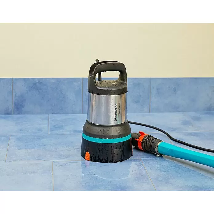 Gardena Klarwasser-Tauchpumpe 17000 Aquasensor - 750 W, Max. Fördermenge: 17.000 l/h - GARDENA 17000 Clear Tauchpumpe, silber, schwarz und türkis, mit blauem Schlauch, auf nassem blauen Fliesenboden.