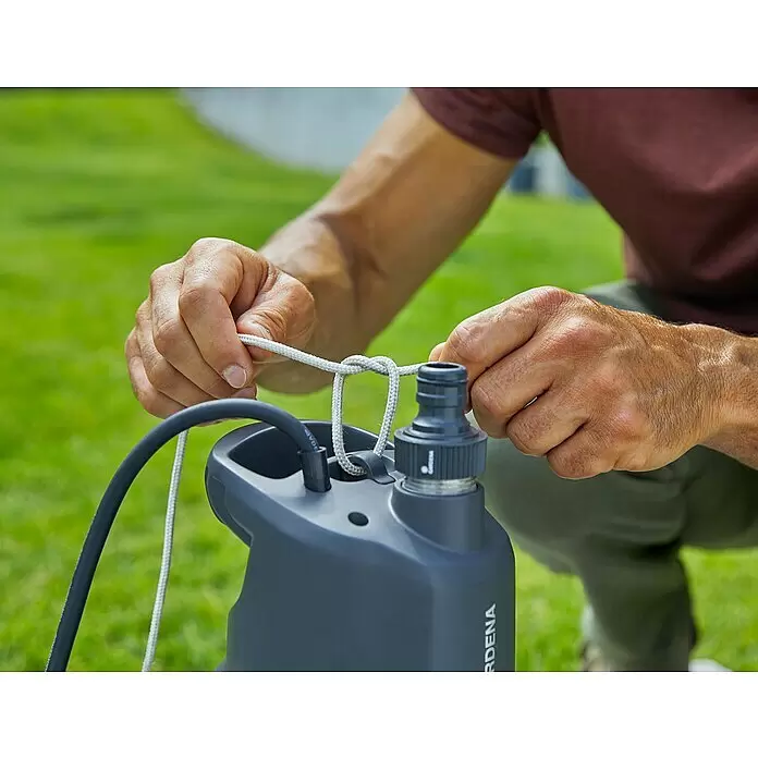 Gardena Drucktauchpumpe 5900/4 Inox - 900 W, Max. Fördermenge: 5.900 l/h - Hände befestigen ein weißes Seil an einer dunkelgrauen GARDENA Pumpe mit angeschlossenem schwarzem Schlauch.