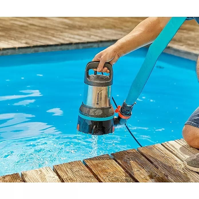 Gardena Klarwasser-Tauchpumpe 11000 Aquasensor - 450 W, Max. Fördermenge: 11.000 l/h - Eine Hand führt eine silberne, schwarze und türkisfarbene GARDENA 11000 Clear Tauchpumpe mit türkisfarbenem Schlauch in ein blaues Becken; Wasser tropft.