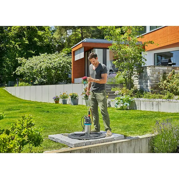 Gardena Drucktauchpumpe 5900/4 Inox - 900 W, Max. Fördermenge: 5.900 l/h - Ein Mann bedient eine Gardena Schmutzwasser-Tauchpumpe 9000 im Garten, um Wasser abzupumpen. Ideale Lösung für Hausbesitzer zur Entwässerung.