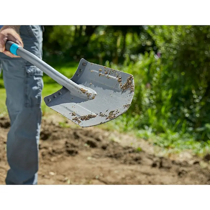 Gardena Ergoline Gärtnerspaten - Mit Tritt, 117 cm - Nahaufnahme eines Schaufelblatts mit Erde, gehalten von einer Person in einem Garten. Das Werkzeug ist bereit für die Gartenarbeit.