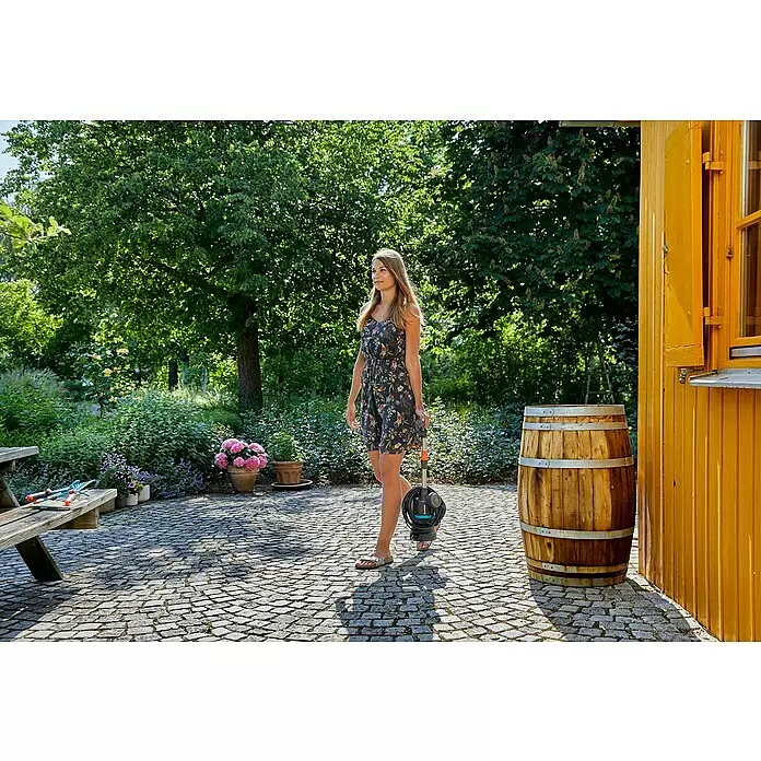 Gardena Regenfasspumpe 4000/1 - 400 W, Max. Fördermenge: 4.000 l/h - Frau trägt eine schwarz-graue Gardena Tauchpumpe mit Schlauch auf gepflasterter Terrasse, bereit für den Garteneinsatz.