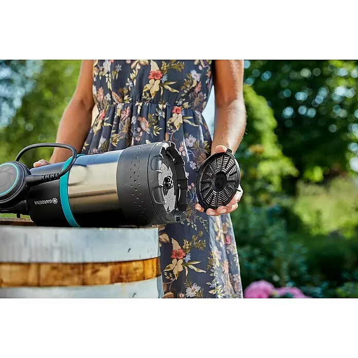 Gardena Regenfasspumpe 4700/2 INOX - 550 W, Max. Fördermenge: 4.700 l/h - Eine Person hält den Filter einer schwarz-silbernen Gardena Pumpe mit türkisen Akzenten, zur Wartung auf einem Holzfass.
