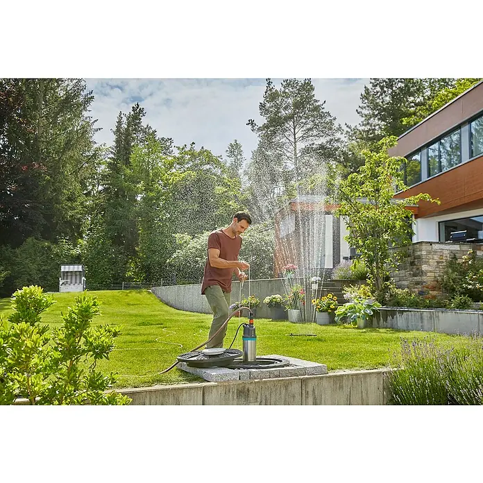 Gardena Tauchpumpe 5900/4 INOX Automatic - 900 W, Max. Fördermenge: 5.900 l/h - Ein Mann bedient eine Gardena-Gartenpumpe, die Wasser verspritzt, während er seinen Garten bewässert.