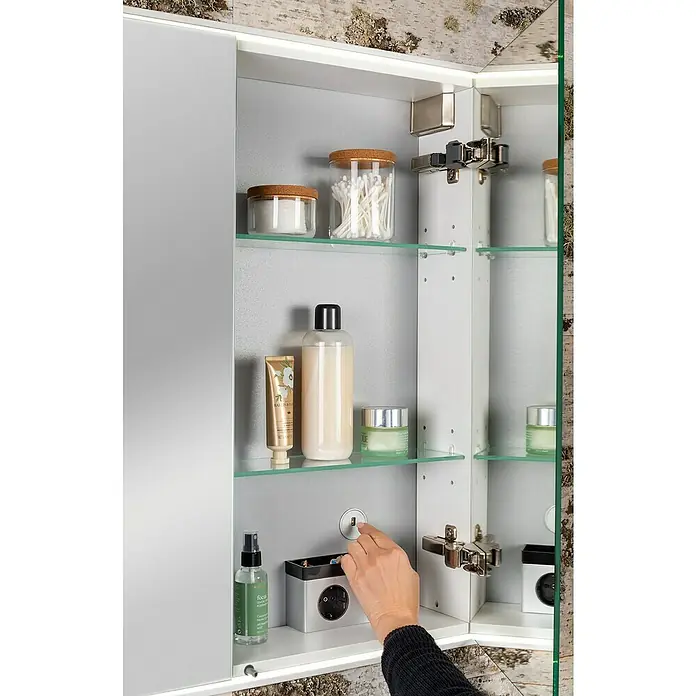 Lanzet Dune LED-Spiegelschrank - B x H: 101,8 x 70,2 cm, Holz, Schwarz - Ein Spiegelschrank mit Kosmetikprodukten auf Glasböden und einer Hand, die einen Schalter betätigt.