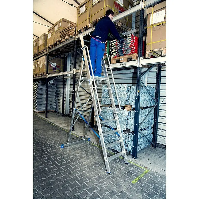 Krause Stabilo Stehleiter - Anzahl Tritte: 8 Stk., Arbeitshöhe: 3,9 m, Aluminium, Sicherheitsbügel - Ein Mann steht auf einer silbernen Krause-Treppe in einem Lagerhaus, um an höher gelagerte Waren zu gelangen.