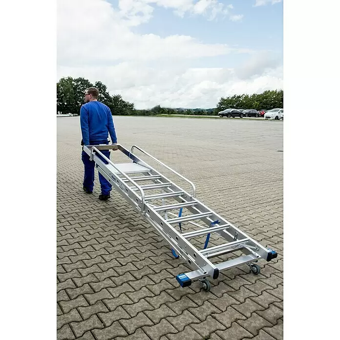 Krause Stabilo Stehleiter - Anzahl Tritte: 8 Stk., Arbeitshöhe: 3,9 m, Aluminium, Handläufe - Mann trägt eine lange, rollbare Aluminiumleiter über einen gepflasterten Bereich. Die Leiter hat blaue Details und Handläufe.