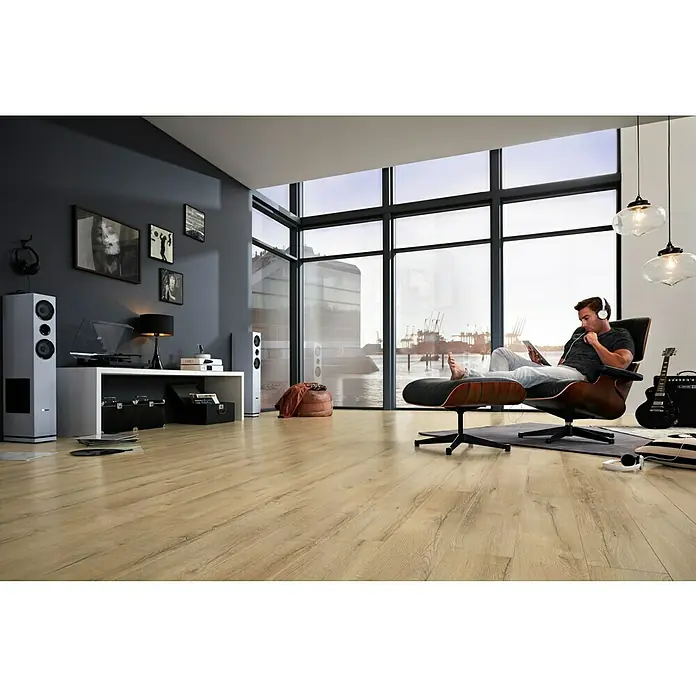 LOGOCLIC Laminado Roble Selva - 1.380 x 193 x 10 mm, Roble Selva, AC5 - Salón con suelo vinílico con aspecto de madera, altavoces, y un hombre relajándose en una silla, escuchando música.