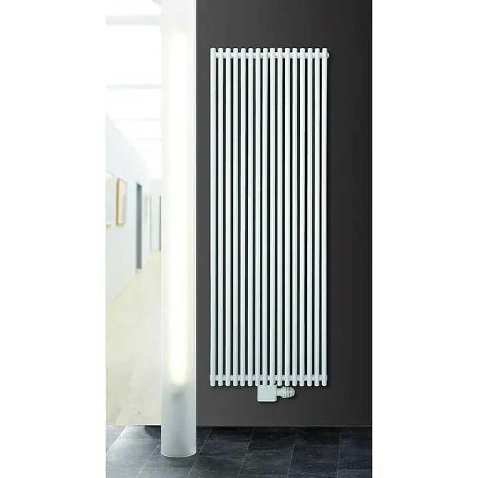 Ximax Raumheizkörper Gamba Duplex - B x H: 470 x 1.800 mm, Wärmeleistung bei Vorlauftemperatur von 75 °C (D: 50): 1.291 W - Das Bild zeigt einen weißen Rippenheizkörper an einer dunklen Wand, neben einer beleuchteten Säule in einem modernen Raum.