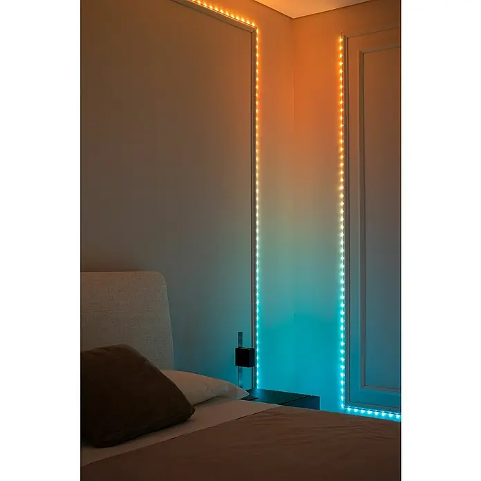 Twinkly Smart-LED-Band Dots - Länge: 10 m, RGB, 24 W, Schwarz - Ein Schlafzimmer mit einem Bett und LED-Lichtern an der Wand, die von Orange nach Blau wechseln, sorgt für eine entspannende Atmosphäre.
