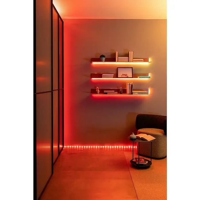 Twinkly Smart-LED-Band Dots - Länge: 10 m, RGB, 24 W, Schwarz - Stimmungsvolles Zimmer mit LED-Beleuchtung unter Regalen und entlang des Bodens. Moderne Möbel ergänzen das Ambiente.
