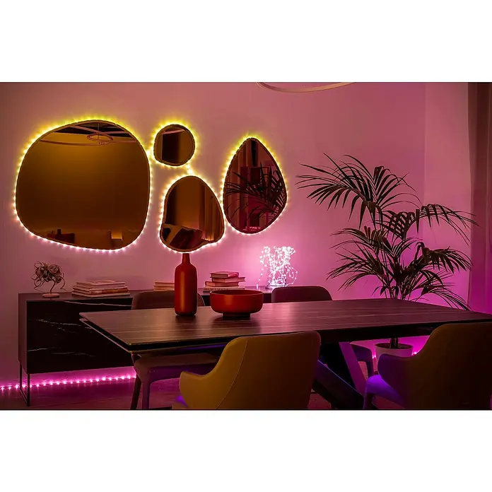 Twinkly Smart-LED-Band Dots - Länge: 10 m, RGB, 24 W, Schwarz - Stimmungsvolles Esszimmer mit LED-beleuchteten, organisch geformten Spiegeln an der Wand und einem modernen Esstisch mit farbigen Akzenten.
