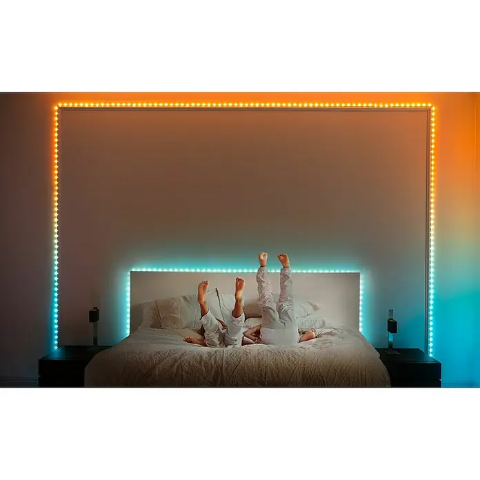 Twinkly Smart-LED-Band Dots - Länge: 10 m, RGB, 24 W, Schwarz - Zimmeransicht mit bunten LED-Leuchten, die einen Rahmen um ein Bett bilden, auf dem zwei Personen mit den Füßen nach oben liegen.