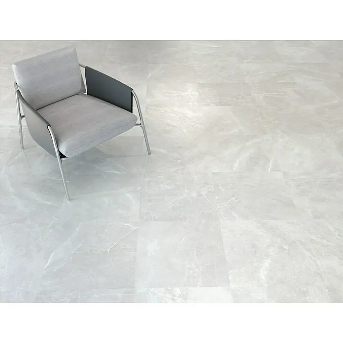 Feinsteinzeugfliese Bayona Silver - 60 x 60 cm, Grau, Glänzend - Ein moderner grauer Sessel auf einem hellen Marmorboden, der eine elegante und minimalistische Atmosphäre erzeugt.