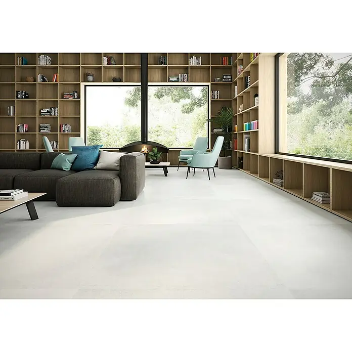 BHS Showroom Pavimento porcelánico Madox - 120 x 120 cm, Blanco, Mate, Rectificado - Elegante salón con sofá gris, estanterías y grandes baldosas blancas en el suelo que dan a la estancia un aspecto moderno.