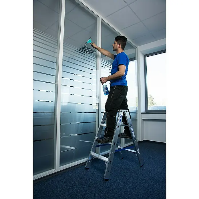 Krause Stabilo Doppelleiter - Anzahl Tritte: 8 Stk., Arbeitshöhe: 2,5 m, Aluminium - Mann reinigt Fenster mit einem Fensterabzieher und Glasreiniger, während er auf einer Krause Leiter steht.