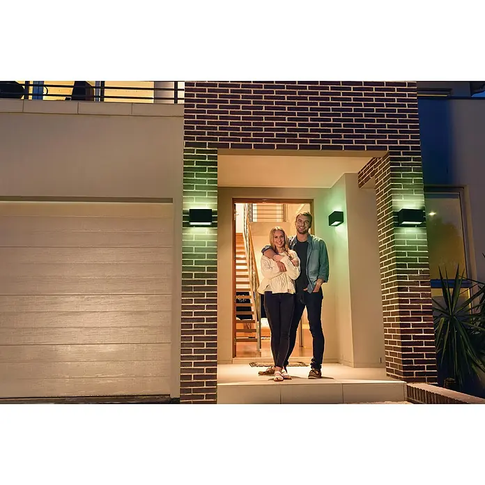 Ledvance Smart+ WiFi LED-Außenwandleuchte Brickwide - Farbe Gehäuse: Dunkelgrau, IP44 - Das Paar steht vor dem Haus, dessen Außenbeleuchtung mit smarten LED-Leuchten akzentuiert wird. Die smarten Leuchten sorgen für eine einladende Atmosphäre.